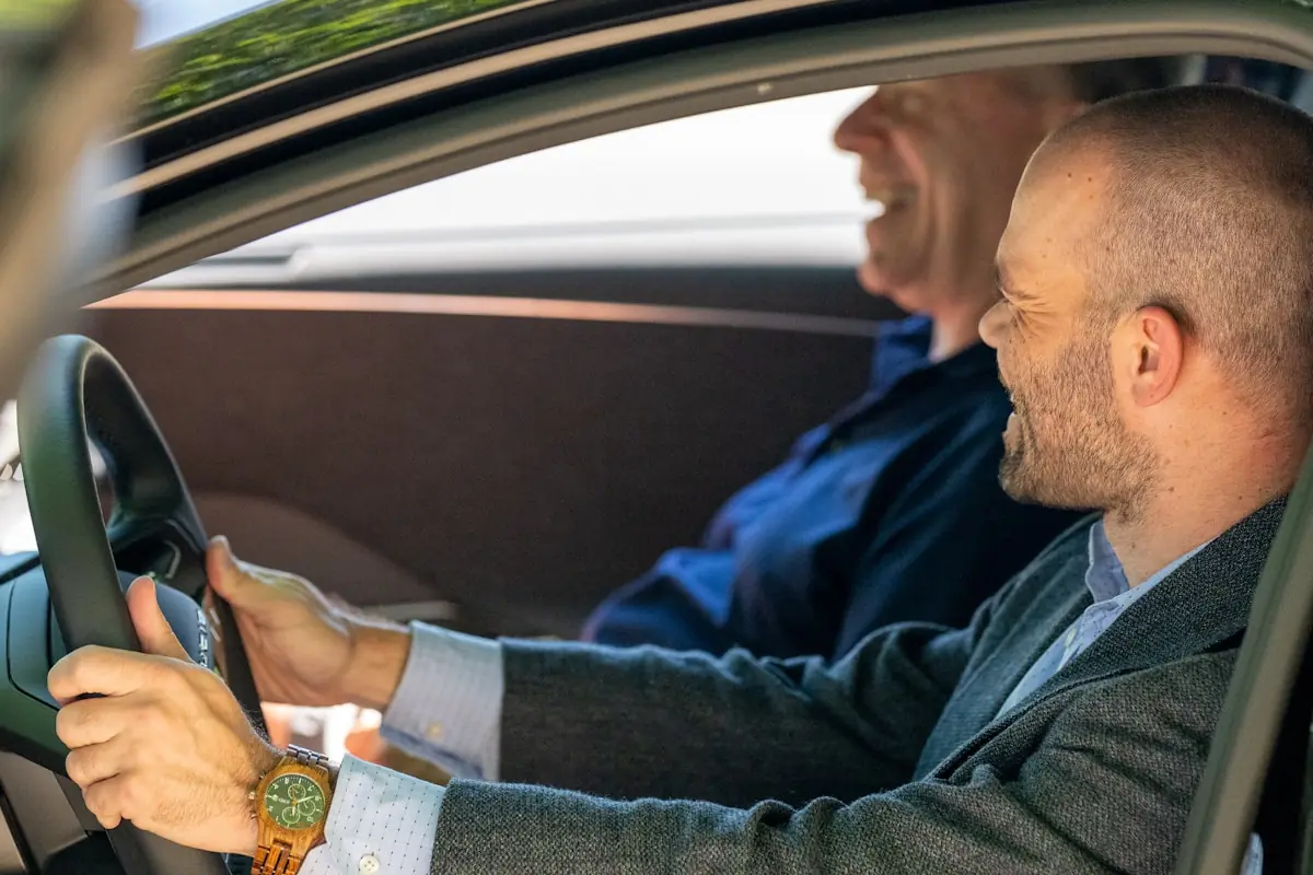 A driving instructor with a clipboard talking with an adult student sitting in the driver's seat