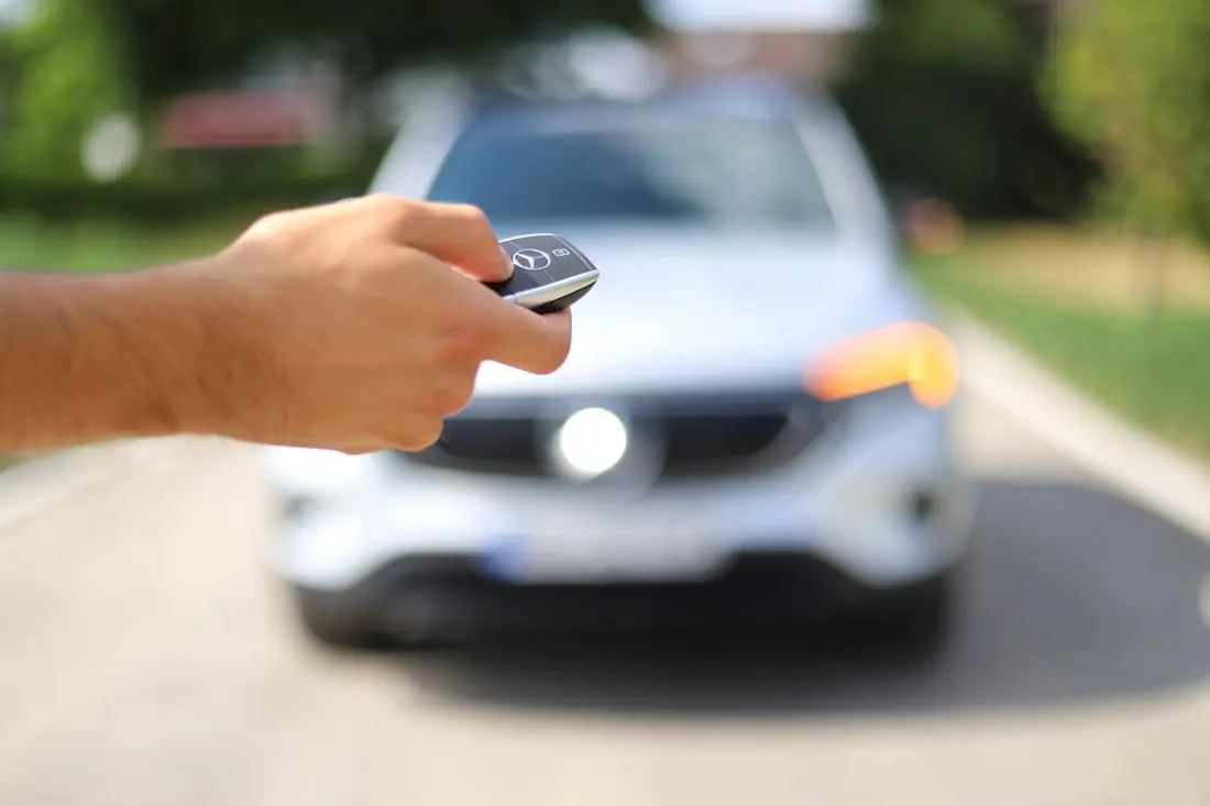 A hand holding a car key fob with a silver car behind